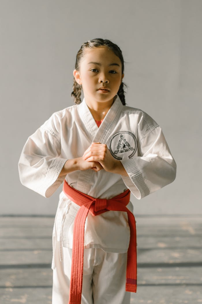 A young girl in a dobok with a red belt, practicing taekwondo indoors during the day.